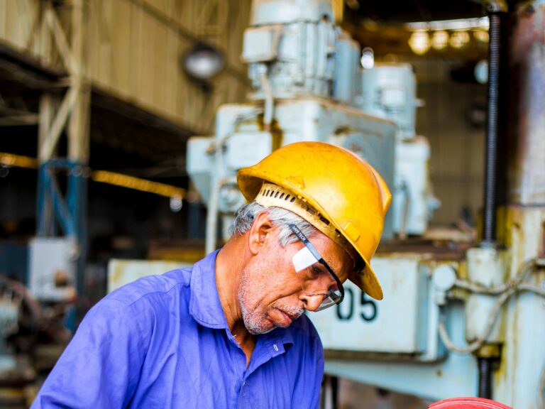 Manufacturing worker in hard hat and safety glasses at an industrial grinder